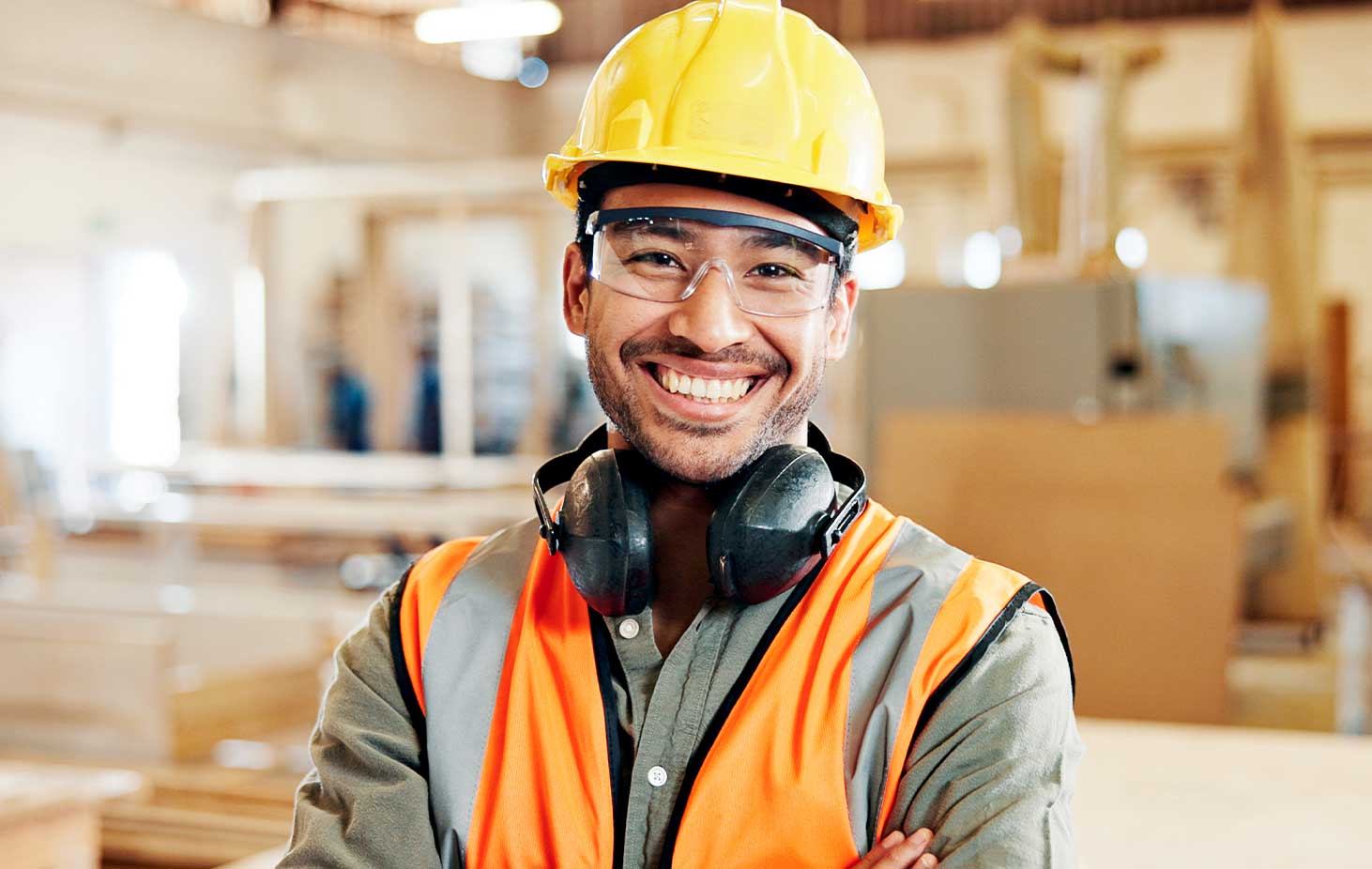 Carpentry, happy and portrait of man in workshop for furniture repair, building and woodworking. Carpenter, safety gear and person with crossed arms in factory for wood, lumber and timber